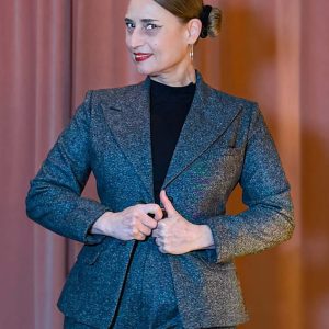 rau in einem grauen Tweed-Hosenanzug bestehend aus dem Blazer Lady Grey und einer weiten Marlene-Hose im Stil der 20er bis 30er Jahre vor einem rosa Vorhang.