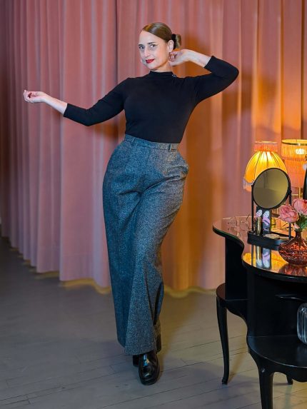 Frau trägt die taillenhohe Marlene-Hose Lady Grey aus grauem Tweed mit Bügelfalten und weitem Bein im Stil der 30er Jahre in einem Vintage-Ambiente.