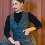 Eine Frau posiert in einer grauen Tweed-Weste und einer passenden weiten Marlene-Hose im Vintage-Stil der 20er Jahre vor einem Boudoir-Hintergrund.