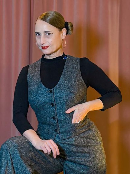 Eine Frau posiert in einer grauen Tweed-Weste und einer passenden weiten Marlene-Hose im Vintage-Stil der 20er Jahre vor einem Boudoir-Hintergrund.