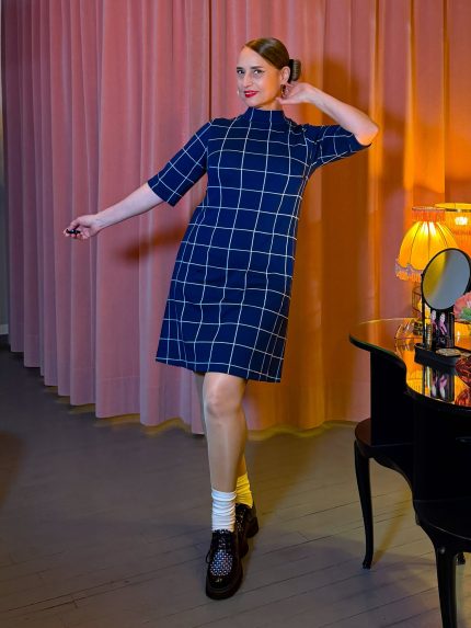 Frau in einem kurzen, navy-blauen Kleid mit weißem Karomuster, Stehkragen und halblangen Ärmeln.