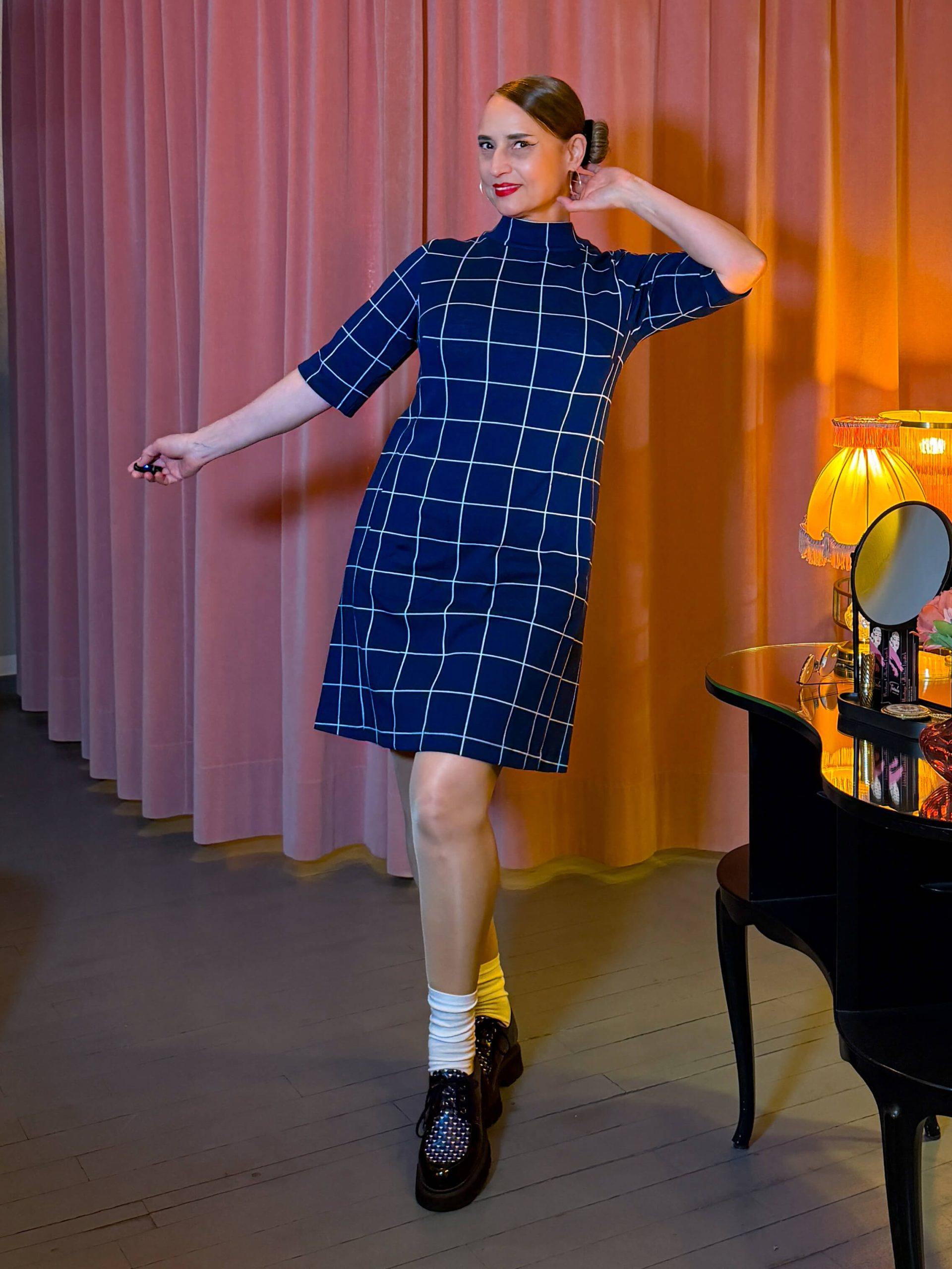 Frau in einem kurzen, navy-blauen Kleid mit weißem Karomuster, Stehkragen und halblangen Ärmeln.