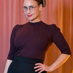 Frau trägt das auberginefarbene Hazel Shirt mit Stehkragen und Dreiviertelärmeln vor einem vintage pinken Samtvorhang.