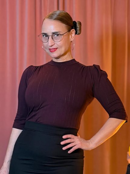 Frau trägt das auberginefarbene Hazel Shirt mit Stehkragen und Dreiviertelärmeln vor einem vintage pinken Samtvorhang.