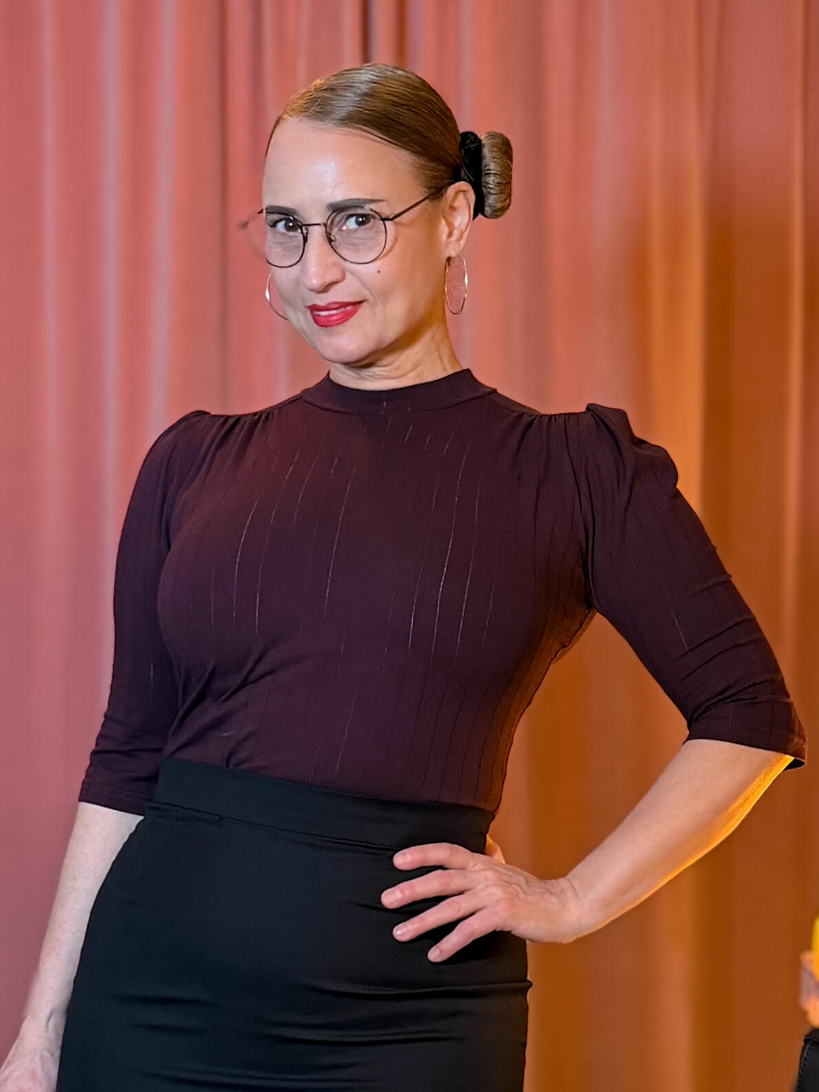 Frau trägt das auberginefarbene Hazel Shirt mit Stehkragen und Dreiviertelärmeln vor einem vintage pinken Samtvorhang.