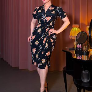 Frau im Mabel Dress, ein schwarzes Vintage-Kleid mit floralem Muster, Wasserfall-Volant und V-Ausschnitt im Park.