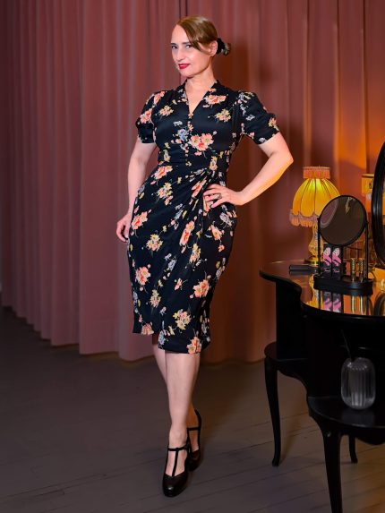 Frau im Mabel Dress, ein schwarzes Vintage-Kleid mit floralem Muster, Wasserfall-Volant und V-Ausschnitt im Park.