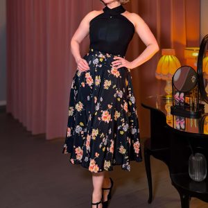 Eine Frau wirbelt in einem weit schwingenden, floralen Isabelle Skirt im 40er Jahre Stil, kombiniert mit einem schwarzen Neckholder Top.