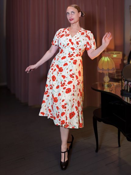 Elegantes Teekleid im Stil der 40er Jahre mit rotem Mohnblumen-Print auf cremefarbenem Viskosestoff, präsentiert in einer stilvollen Boudoir-Atmosphäre mit Vintage-Lampe und Klavier – perfekt für einen sommerlichen Nachmittagsempfang – Hazel's Boudoir